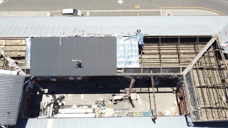 Overhead view of new dark roof sheeting beside exposed framing and reflective underlay